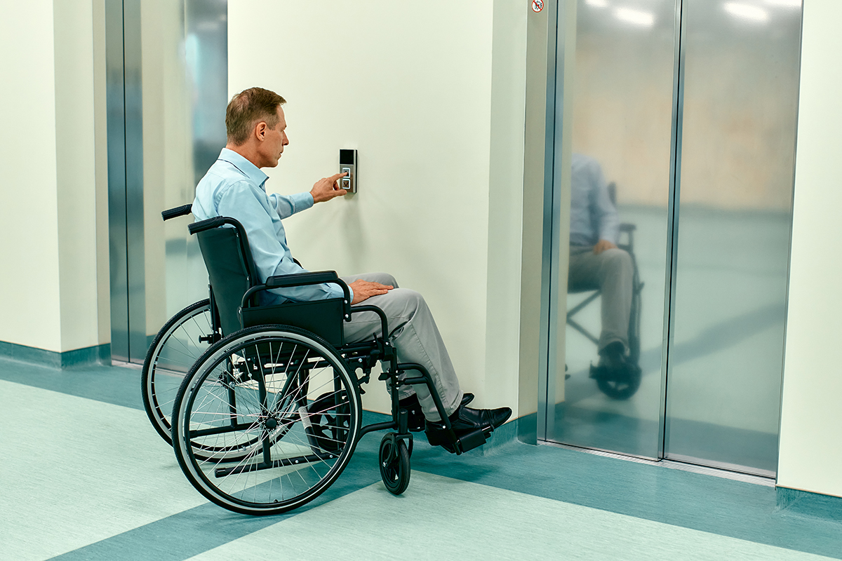 An elderly disabled man in a wheelchair presses the call button